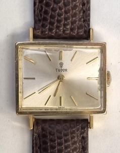 Rolex Tudor manual wind wrist watch in a rectangular 18K gold case with Swiss proof marks on a brown textured leather strap with gilt buckle. Signed silvered dial with gilt baton hours and matching polished gilt hands. Swiss made signed Tudor calibre 2424 17 jewel jewelled lever movement with gold case back internally numbered 548716 and externally marked 1960.