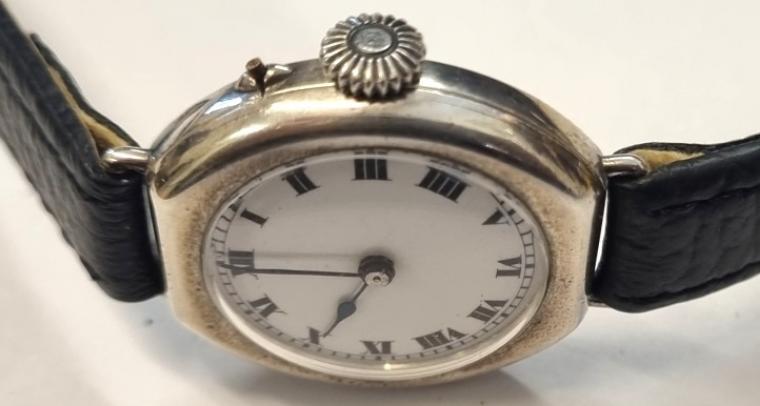 Swiss tonneau shaped Officers Style Trench wrist watch in a silver case with London import hallmark for c1923 on a black leather strap with silvered buckle. Crown manual wind with separate pin set time change. White enamelled dial with black Roman hours and minute track and blued steel hands. Swiss jewelled lever movement with case back by 'G.D' and numbered 366741 2.