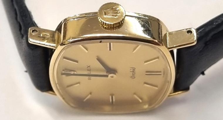 Ladies Rolex Orchid wrist watch in an 18K gold case with Swiss proof marks on a black leather strap with gilt buckle. Signed champagne coloured dial with baton hour markers and matching black hands. Swiss Rolex signed 18 jewel jewelled lever calibre 1400 hand wind movement with signed and numbered case back.