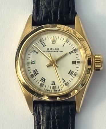 Ladies Rolex Oyster Perpetual wrist watch in a signed 18K gold case with Swiss proof marks on a leather strap with gilt buckle. Signed white dial with black Roman hours and gold indices with polished gilt hands and centre seconds. Swiss Rolex signed 28 jewel jewelled lever calibre 2300 Chronometer movement with screw down crown and Oyster case back.