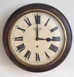 English Smiths of Enfield oak cased 8 day dial clock time piece c1940s. Circular oak case with brass bezel and flat glass door over a 12" white dial with black Roman hours and black steel hands and single winding square. 8 day spring driven, pendulum regulated movement with recoil anchor escapement and open going barrel accessed via a lower case opening door. Case Dimensions: Diameter - 16", Depth - 5".