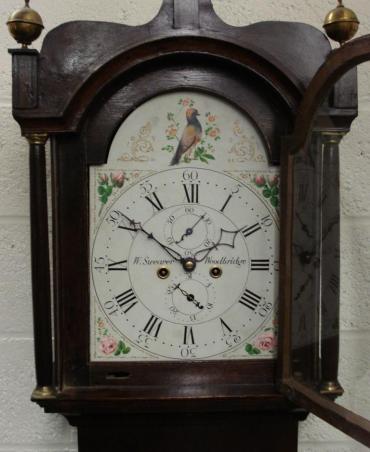 Dark stained oak case with brass globe finials, grandfather longcase clock. Ogee topped hood with brass terminal fluted pillars and decorative painted face. Bell striking, 8 day movement circa 1830, with seconds indication and date display, signed to the dial W Swearer, Woodbridge.