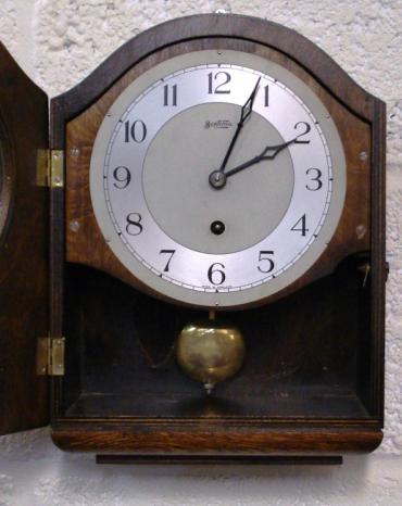Stained oak cased 8 day spring driven pendulum regulated kitchen clock by Bentima circa 1950, with decorative wooden moulding and visible pendulum. Silvered two tone dial with Arabic hours and matching blued steel hands. Case height - 13".