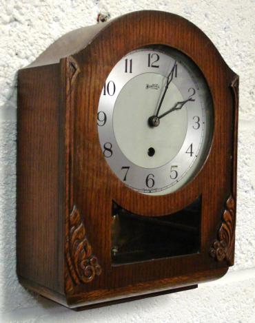 Stained oak cased 8 day spring driven pendulum regulated kitchen clock by Bentima circa 1950, with decorative wooden moulding and visible pendulum. Silvered two tone dial with Arabic hours and matching blued steel hands. Case height - 13".