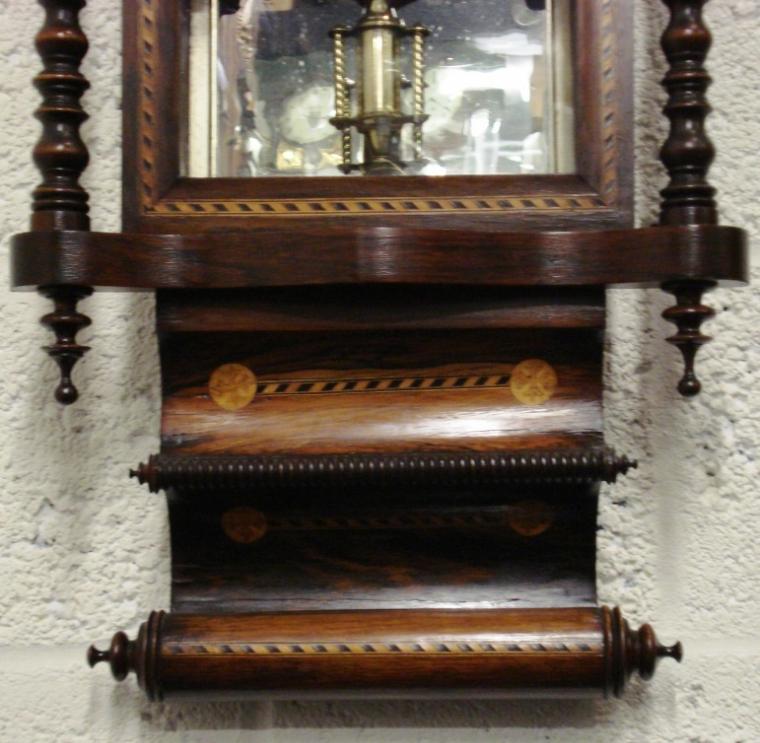 American 8 day bell striking spring driven pendulum movement, housed in a very decorative mahogany veneer case, with ebony and boxwood stringing. Fretwork dial surround with red damask lining over a mirror glass interior and ornate brass and steel pendulum. White painted dial with black roman hour markers and black painted steel hands.
