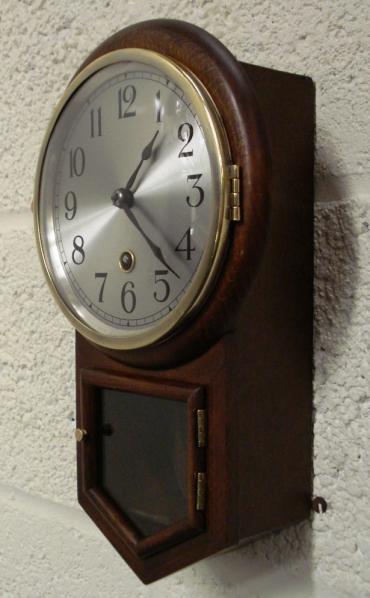 German dark oak drop dial cased wall clock by H.A.C. of Wurttemberg. Brass bezel with convex glass over a silvered dial with black arabic numerals and black painted steel hands. Separate opening window to visible brass pendulum and key holder. H.A.C. paper label on clock back with number #2609.