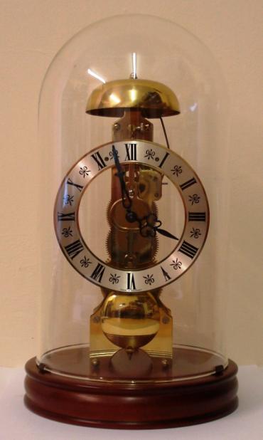 Modern German Hermle '82' 8 day skeleton clock. Glass dome over wood effect base, silvered dial with black painted roman hour markers and black painted hands. Spring driven in line pendulum movement with passing strike on a bell.