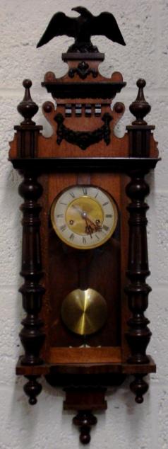 German 8 day gong striking wall clock circa 1900, spring driven pendulum movement housed in an oak and pine case with decorative turned finials and side columns together with applied swags and surmounted by an eagle. Ivory and brass coloured dial with black roman hour markers and black steel hands, and an enamel pendulum regulation plate at the case bottom.  Dimensions - Height 40", Width 13", Depth 7.5".