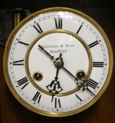 German 8 day wall clock circa 1880, spring driven pendulum movement housed in a pine case with a decorative turned finial and side columns together with applied mouldings. White enamel and brass dial with black roman hour markers and black steel hands, the dial signed 'Fattorini & Sons, Bradford' and 'Made in Baden'. The movement has a banjo style pendulum and there is an enamel pendulum regulation plate at the case bottom. Unusually the movement does not strike the hours or half hours, but plays an air on a musical box mechanism on the hour 