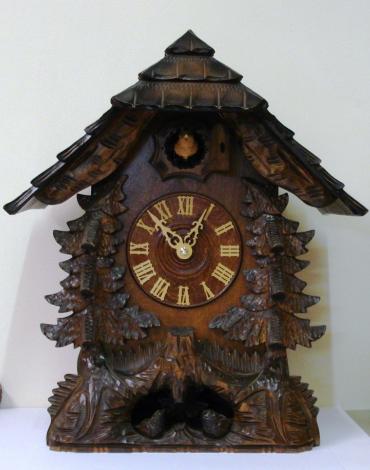 New quartz mantel / wall cuckoo clock by Harzer. Pine wood case with stylised pine tree decoration and nesting bird motif. Traditional carved light coloured wood chapter ring with roman hours and matching wooden hands. Visible pendulum and carved light wood cuckoo bird display on the hour