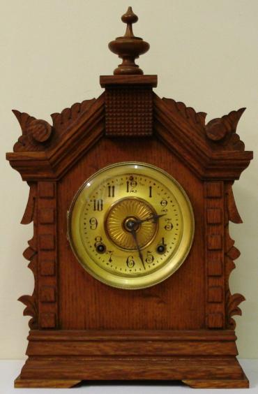 American oak cased 8 day bracket clock by the Ansonia Clock Co. circa 1900. Architectural heavily carved wooden case with turned finial and bracket feet. Circular gilt brass bezel with flat chamfered glass over matt gilt dial with slow / fast regulation at 12 o'clock with black arabic hours and ornate black steel hands. Skeleton square brass gong striking spring driven, pendulum regulated, movement stamped with 'Ansonia Clock Co, New York, USA' and 'Patented June 18,1882'.
