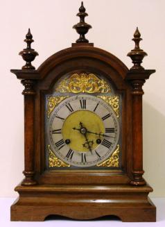 Fruit wood and pine cased 8 day bracket clock circa 1900. Dome topped case with turned finials and side columns on a solid plinth base. Front opening casework with flat glass over steel dial plate with applied gilt spandrels and gilt winged angel head decoration. Silvered chapter ring with matt gilt brass centre and black roman hours with decorative blued steel hands. Square brass gong striking, spring driven, pendulum regulated movement, maker unknown but numbered to the back plate #82449. Dimensions: Height - 16", width - 10.5", depth - 7"
