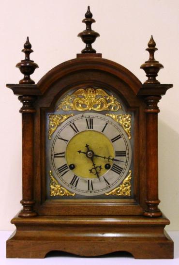 Fruit wood and pine cased 8 day bracket clock circa 1900. Dome topped case with turned finials and side columns on a solid plinth base. Front opening casework with flat glass over steel dial plate with applied gilt spandrels and gilt winged angel head decoration. Silvered chapter ring with matt gilt brass centre and black roman hours with decorative blued steel hands. Square brass gong striking, spring driven, pendulum regulated movement, maker unknown but numbered to the back plate #82449