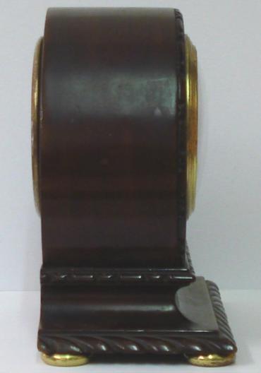 French 8 day mantel timepiece circa 1920 with round top dark mahogany case with carved plinth decoration and gilt bun feet. Gilt brass bezel with convex glass over a silvered dial with engine turned centre and black arabic hours and black steel hands. Brass drum movement with contemporary cylinder escapement platform, and stamped 'Made in France' with a captive winding key.