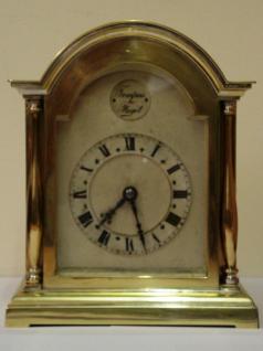 French 8 day brass cased mantel clock timepiece circa 1910. Dome topped case with decorative brass side pillars and ornate rear door hinge. Cutout brass front plate with flat glass over silvered dial plate with black roman hours and ornate black steel hands. Circular French brass drum movement, maker unknown. with lever escapement and captive winding key.  Dimensions: Height - 7.25", width - 6", depth - 4".