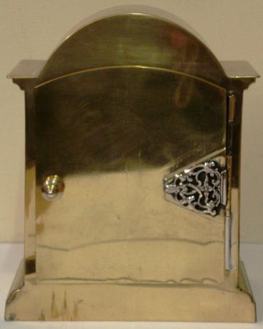 French 8 day brass cased mantel clock timepiece circa 1910. Dome topped case with decorative brass side pillars and ornate rear door hinge. Cutout brass front plate with flat glass over silvered dial plate with black roman hours and ornate black steel hands. Circular French brass drum movement, maker unknown. with lever escapement and captive winding key.