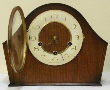 English 8 day oak veneer cased mantel clock circa 1950 by Smiths. Angular round topped case with delicate side moulding and a circular brass bezel with convex glass over an ivory coloured chapter ring. Gilt arabic hours and fretwork hands and Chime / Silent control at 9 o/c. Good quality pendulum regulated, spring driven, rod striking brass movement with decorative engine turning and stamped '-Smiths-, Made in Great Britain, Smiths English Clocks Ltd.'.