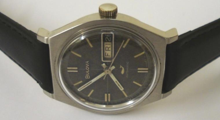 Bulova automatic wrist watch in a stainless steel case on a black leather strap with silver buckle. Aged dark blue dial with silvered baton hour markers and matching hands with sweep seconds hand and day / date display at 3 o/c. Swiss made Bulova calibre 11ANACB 17 jewel automatic movement circa 1965, with screw on case back numbered M9 G971526.