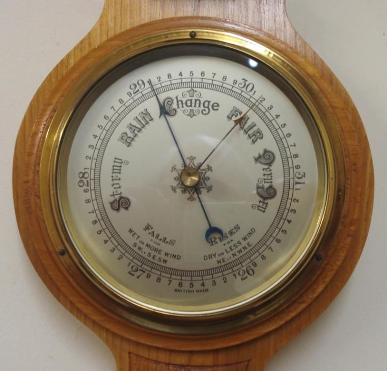 British aneroid barometer in a light oak solid wood carved and moulded case circa 1930s. Circular brass bezel with chamfered glass over a silvered dial with black painted pressure index, blued steel pressure indicator and brass history pointer. Separate red alcohol Fahrenheit and Centigrade thermometer.  Dimensions: - Height 22.5", width 7", depth 2.5". 