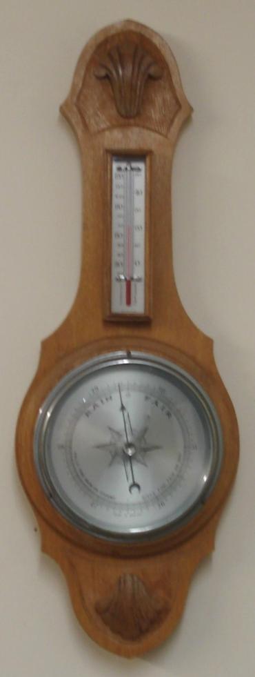 English aneroid barometer in a light oak solid wood carved and moulded case circa 1930s. Circular chromed bezel with chamfered glass over a silvered dial with black painted pressure index, blued steel pressure indicator and silvered history pointer. Separate red alcohol Fahrenheit and Centigrade thermometer.  Dimensions: - Height 19.5", width 7", depth 3".