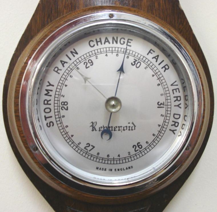 English aneroid barometer in a dark stained oak solid wood carved and moulded case by Renneroid circa 1930. Circular chromed bezel with chamfered glass over a silvered dial with black painted pressure index, blued steel pressure indicator and silvered history pointer. Separate mercury Fahrenheit and Centigrade thermometer.  Dimensions: - Height 18.5", width 5.5", depth 3".