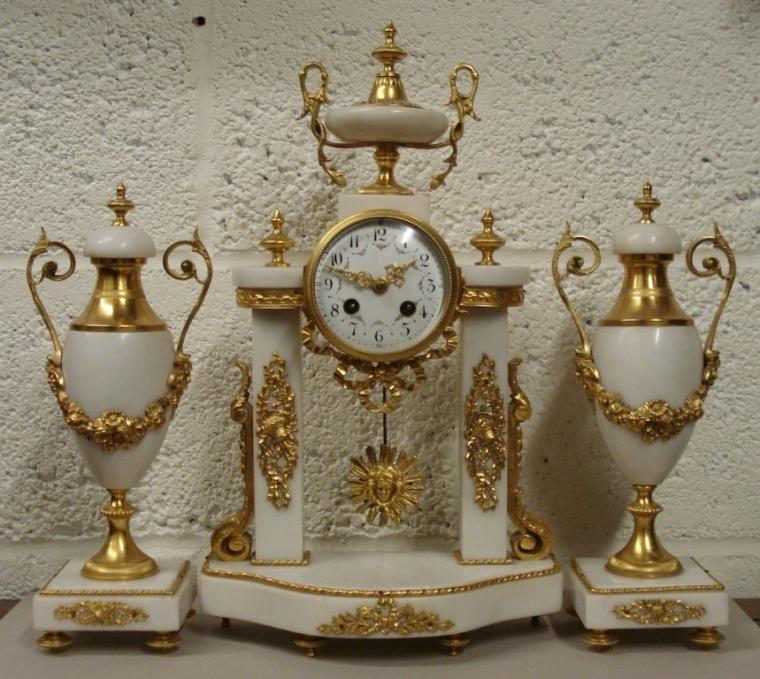 French 8 day bell striking white marble clock garniture circa 1880, maker unknown. Classically styled in ornate ormolu decorated white marble with two lidded urns and central column supported drum case clock. Gilded bezel with concave chamfered glass over a white enamel dial with black Arabic hours and floral swags, gilded hands and two winding squares with slow/fast regulator at 12 o/c. Good quality brass drum shaped spring driven, pendulum regulated movement striking on a silvered bell and numbered #3790.  Clock Dimensions - Height 17", Width 10", Depth 5".