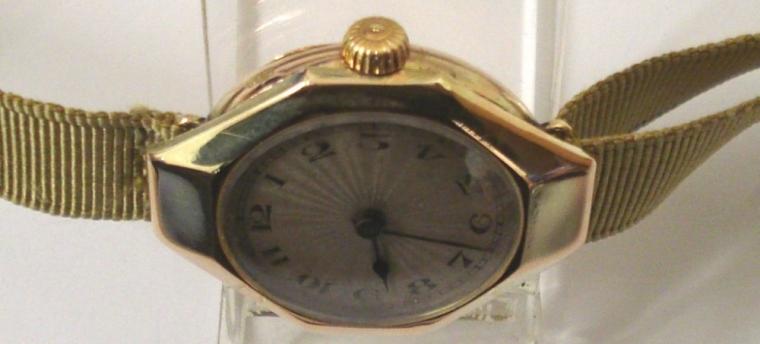 Ladies vintage Rolex manual wind wrist watch in an octagonal 9ct gold case on a gold coloured fabric strap with gilt fastening. Silvered radial dial with black Arabic hour markers and blued steel hands. Signed Rolex jewelled lever movement with Rolex case numbered #1158006 and import hallmarked for London circa 1921.