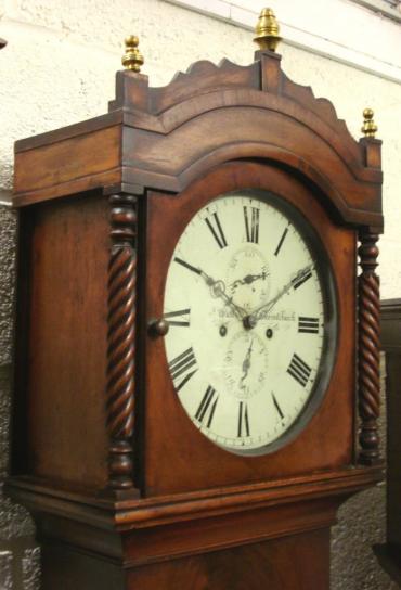 English 8 day bell striking, weight driven and pendulum regulated longcase clock by Watts of Christchurch circa 1840. Substantial flame mahogany veneered casework with domed top, barley twist pillars and brass finials and lower weight and pendulum access door. Signed round white painted dial with Roman hours and silvered hands with seconds and date display subsidiary dials.  Dimensions - Height 86", Width 19.5", Depth 10".
