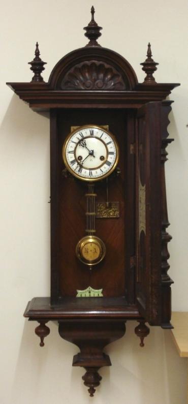 German H.A.C. of Wurttemberg 8 day 'ting tang' wall clock in an ornate heavily carved and moulded walnut case with finials and a full length glazed door. Decorative brass bezel with a white enamel dial with black Roman hours and ornate black gothic hands. In view faux gridiron pendulum with lower enamel adjustment index. Signed spring driven, pendulum regulated 'ting tang' quarter striking movement, circa 1890.  Dimensions: Height - 40.5", Width - 16.5", Depth 8.5".