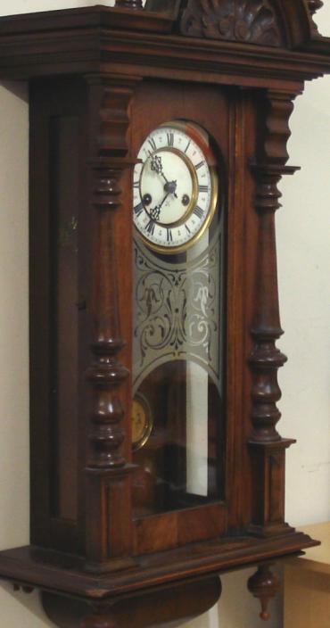 German H.A.C. of Wurttemberg 8 day 'ting tang' wall clock in an ornate heavily carved and moulded walnut case with finials and a full length glazed door. Decorative brass bezel with a white enamel dial with black Roman hours and ornate black gothic hands. In view faux gridiron pendulum with lower enamel adjustment index. Signed spring driven, pendulum regulated 'ting tang' quarter striking movement, circa 1890.  Dimensions: Height - 40.5", Width - 16.5", Depth 8.5".