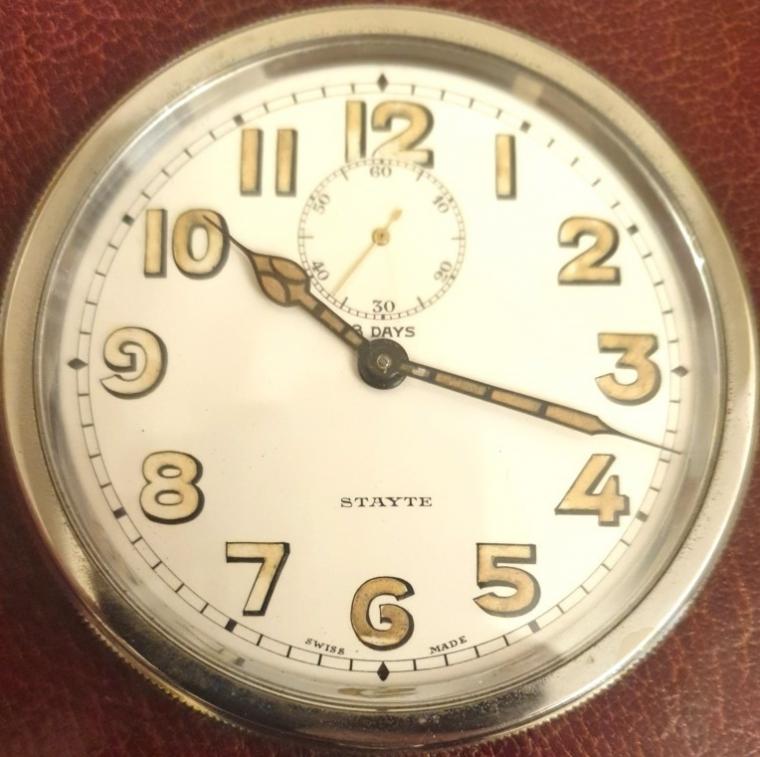 Swiss 8 day bedside travel watch by Stayte in a burgundy leather fold up travel case circa 1920. Bottom wind and time change with white enamel dial and black Arabic luminous insert hours with matching pierced blued steel hands and subsidiary seconds dial at 12 o/c. Swiss made 7 jewel adjusted jewelled lever movement reference 173, with overcoil hairspring and numbered #1865.