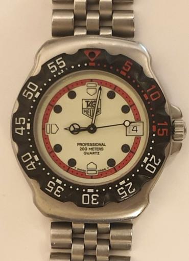 Swiss Tag Heuer Professional midsize quartz F1 watch in a stainless steel case with integral stainless steel bracelet and extending clasp. Black rotating safety bezel with red and white minute markers over a white dial with red minute track and black hour markers. Black luminous insert hands with matching centre seconds hand and date display at 3 o/c, water resistant to 200m.