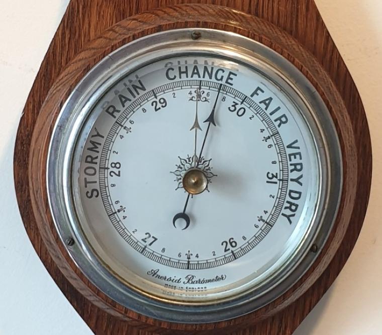 English carved dark oak mounted aneroid barometer and thermometer, circa 1930s. Circular silvered brass bezel with chamfered flat glass over a white dial with black inches of mercury pressure index and a blued steel pressure indicating hand with a gilt history marker hand together with a mercury thermometer displaying temperature in both Fahrenheit and Centigrade.