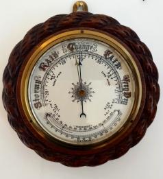 English circular dark wood mounted aneroid barometer with decorative rope twist moulding, early C20th. Circular gilt brass bezel with chamfered flat glass over a white dial with black inches of mercury pressure index and a blued steel pressure indicating hand with a gilt history marker hand together with a mercury thermometer displaying in both Fahrenheit and Centigrade.  Diameter - 7.5", 190mm, depth - 3", 75mm.