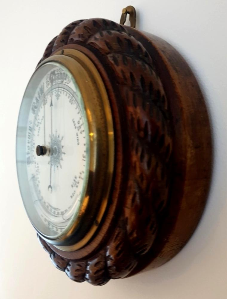 English circular dark wood mounted aneroid barometer with decorative rope twist moulding, early C20th. Circular gilt brass bezel with chamfered flat glass over a white dial with black inches of mercury pressure index and a blued steel pressure indicating hand with a gilt history marker hand together with a mercury thermometer displaying in both Fahrenheit and Centigrade.
