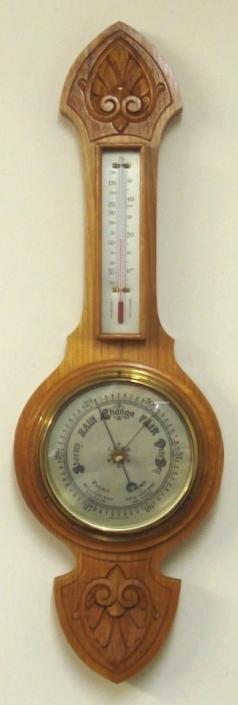 British aneroid barometer in a light oak solid wood carved and moulded case circa 1930s. Circular brass bezel with chamfered glass over a silvered dial with black painted pressure index, blued steel pressure indicator and brass history pointer. Separate red alcohol Fahrenheit and Centigrade thermometer.  Dimensions: - Height 22.5", width 7", depth 2.5". 