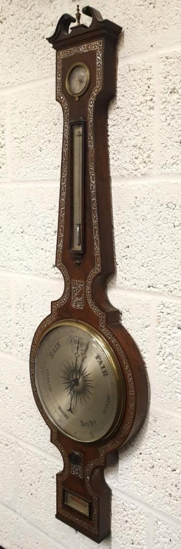 English Georgian rosewood mercury wheel barometer with hygrometer and mercury Fahrenheit thermometer under a swan neck pediment with brass finial and throughout profuse decorative mother-of-pearl inlay. Circular brass bezel with convex glass over a silvered dial engraved with black inches of mercury pressure index and a blued steel pressure indicating hand with a gilt history marker. The alcohol spirit level indicator at the case bottom signed by 'Waymand' of 'Haddenham'.    Height - 45" and width - 13.5".