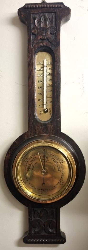 English carved dark oak mounted aneroid barometer and thermometer, circa 1920s. Circular brass bezel with flat glass over a polished brass dial engraved with black inches of mercury pressure index. Black pressure indicating hand with gilt manual history marker together with a brass mounted thermometer displaying temperature in both Fahrenheit and Centigrade. Height - 18" and width - 6.5".